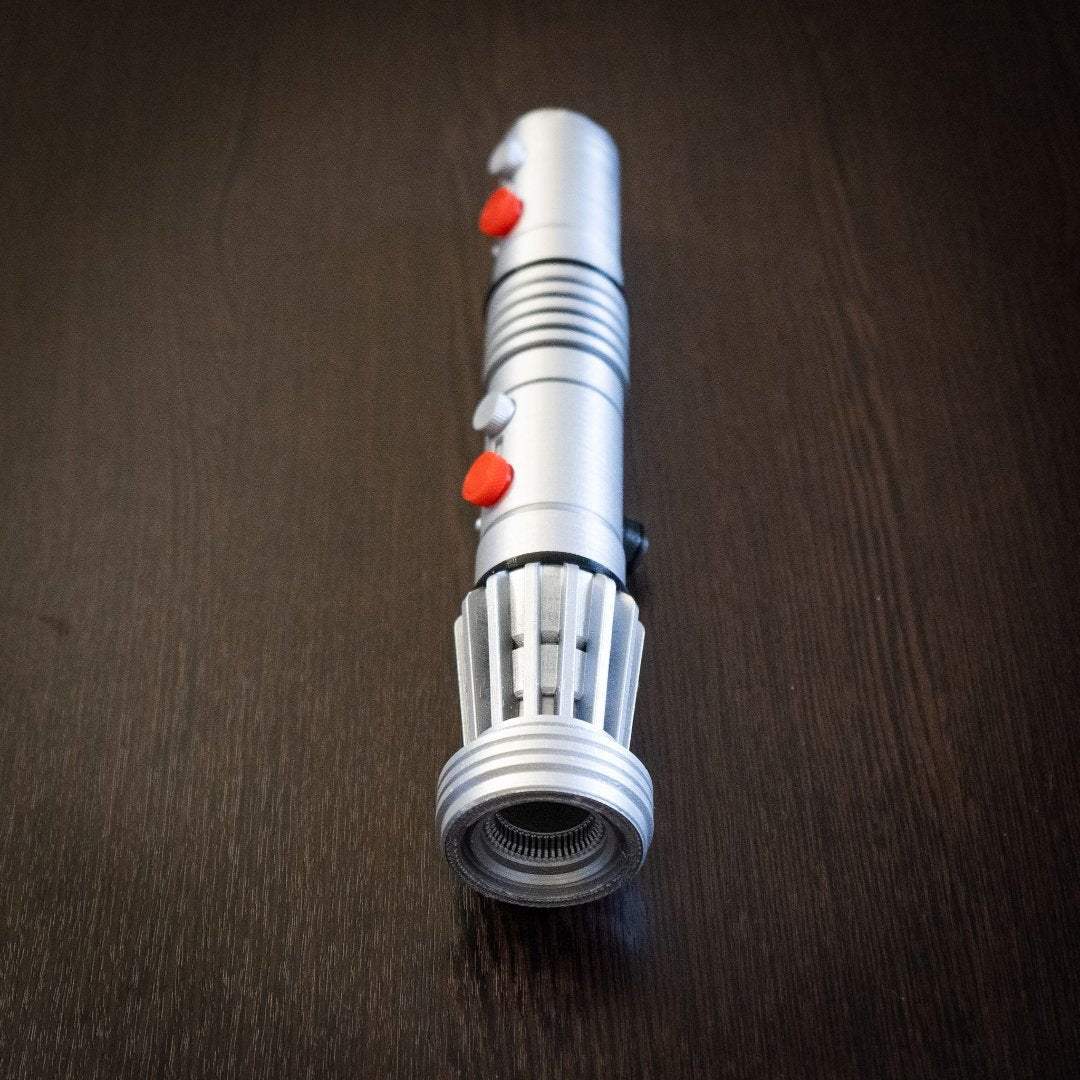 Darth Maul single-bladed lightsaber replica prop in silver with red buttons on dark wood background