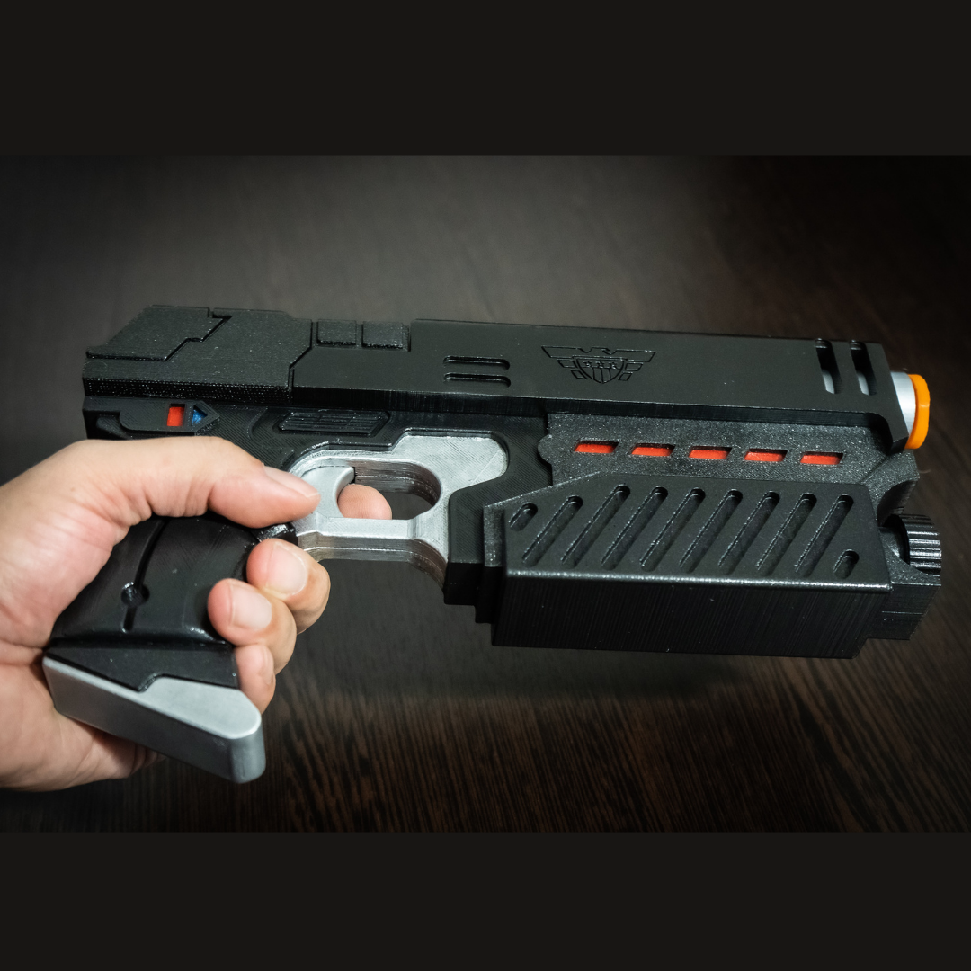 Hand holding a black and silver Judge Dredd Lawgiver cosplay prop gun with orange and red accents on a dark wood surface.