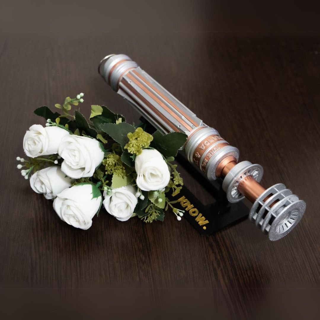 Star Wars inspired bridal bouquet holder designed as Leia Organa's lightsaber in copper and chrome colors holding white roses on dark wooden surface