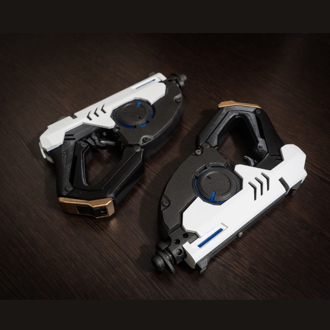 Pair of black and white Tracer's Pulse Pistols cosplay replicas on a dark wooden surface