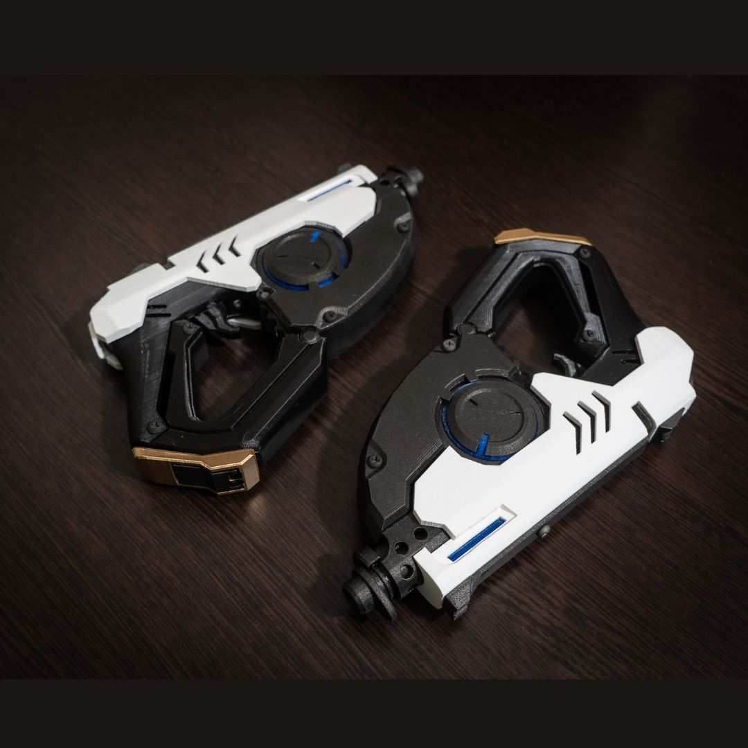 Pair of 3D printed white and black Tracer's Pulse Pistols cosplay replica guns laid on dark wooden surface