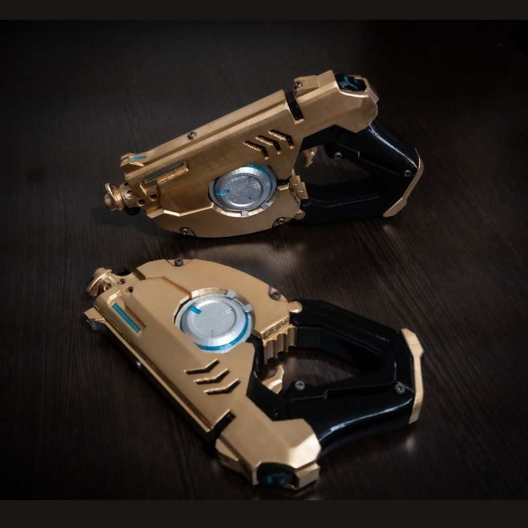 Pair of gold and black Tracer's Pulse Pistols cosplay gun replicas on dark surface