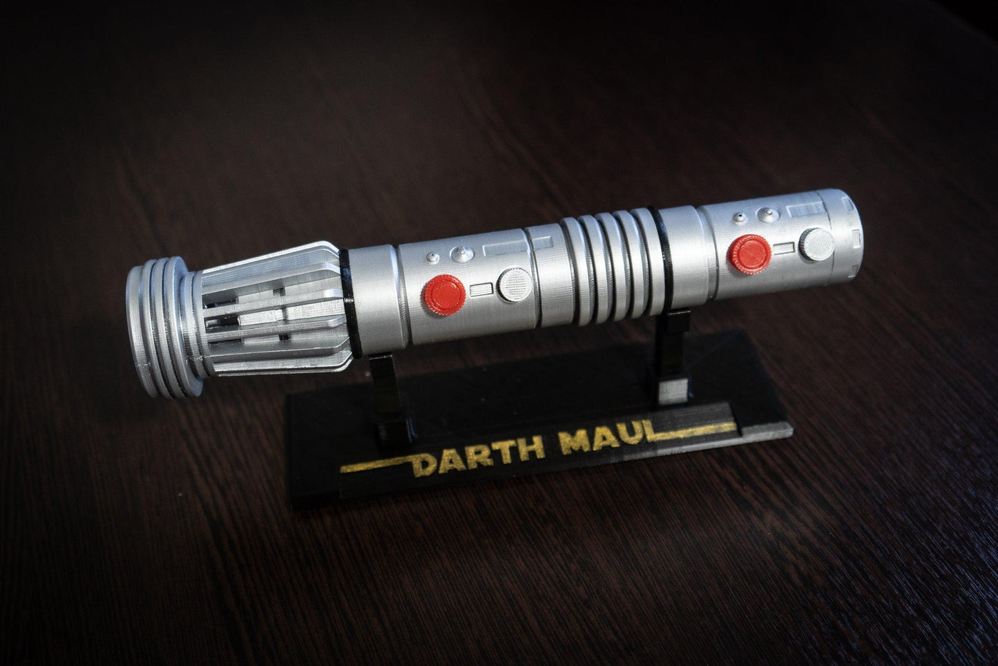 Darth Maul single-bladed lightsaber replica in silver with red buttons on black display stand labeled Darth Maul