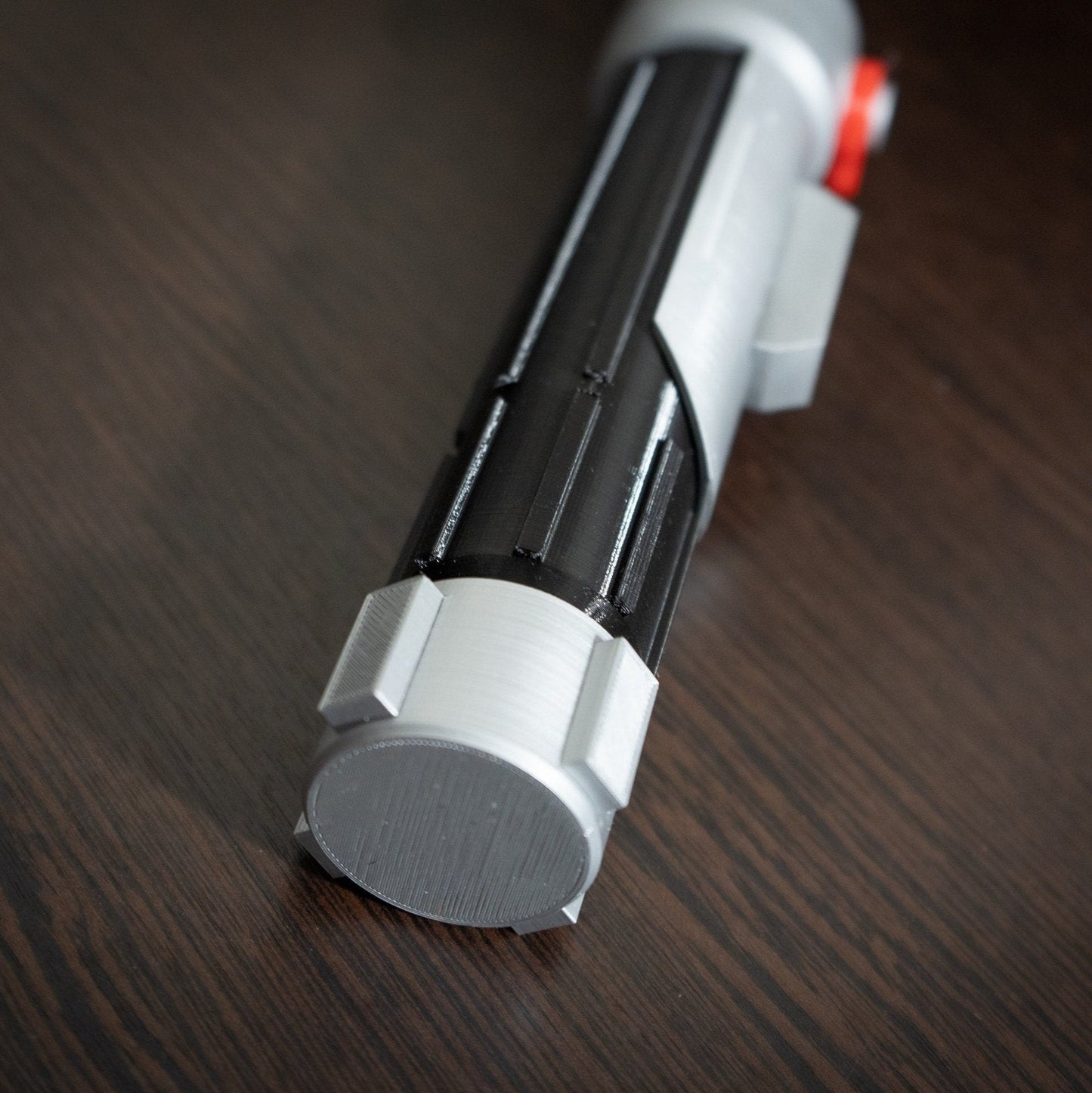 Ezra Bridger second lightsaber hilt Star Wars cosplay prop made of black and silver plastic with red button detail on wooden surface