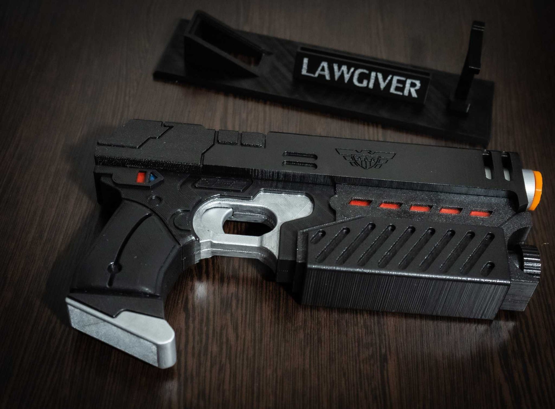 Judge Dredd Lawgiver cosplay prop gun replica with black and silver design and detailed markings on wooden surface.