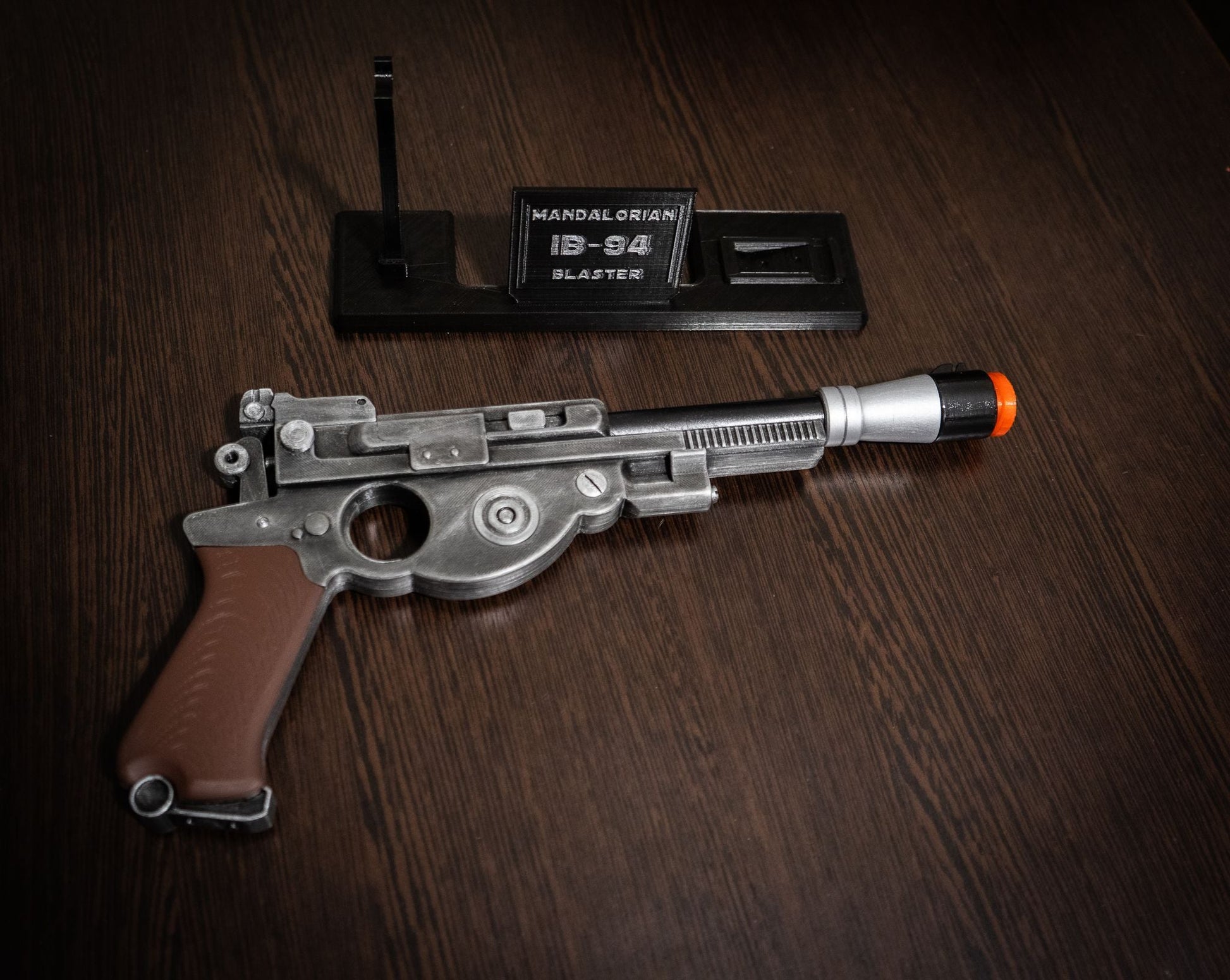Mandalorian Blaster IB-94 Star Wars replica prop gun with orange safety tip and display stand on wooden surface