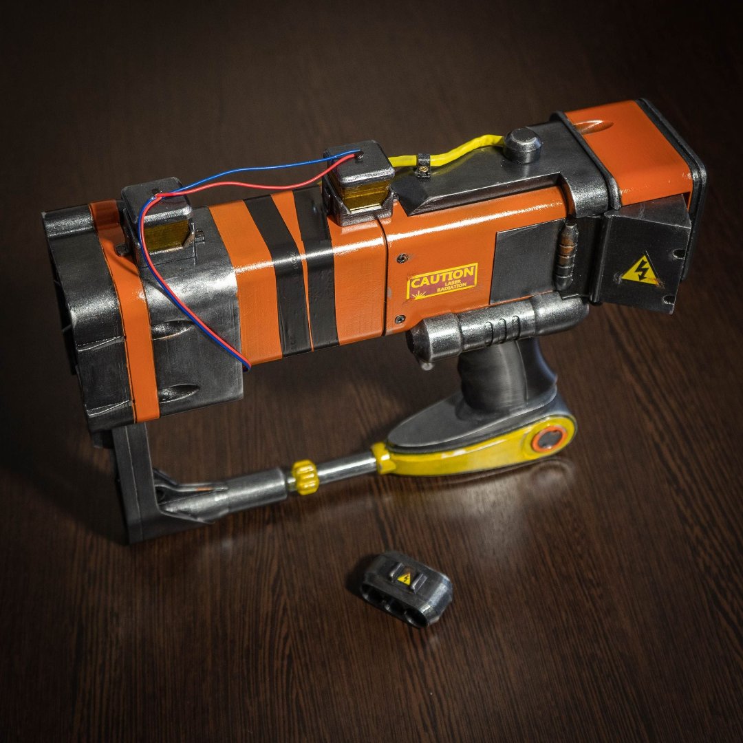 3D printed Fallout New Vegas AEP7 laser pistol cosplay prop with orange and black detailing and caution labels on dark wooden surface