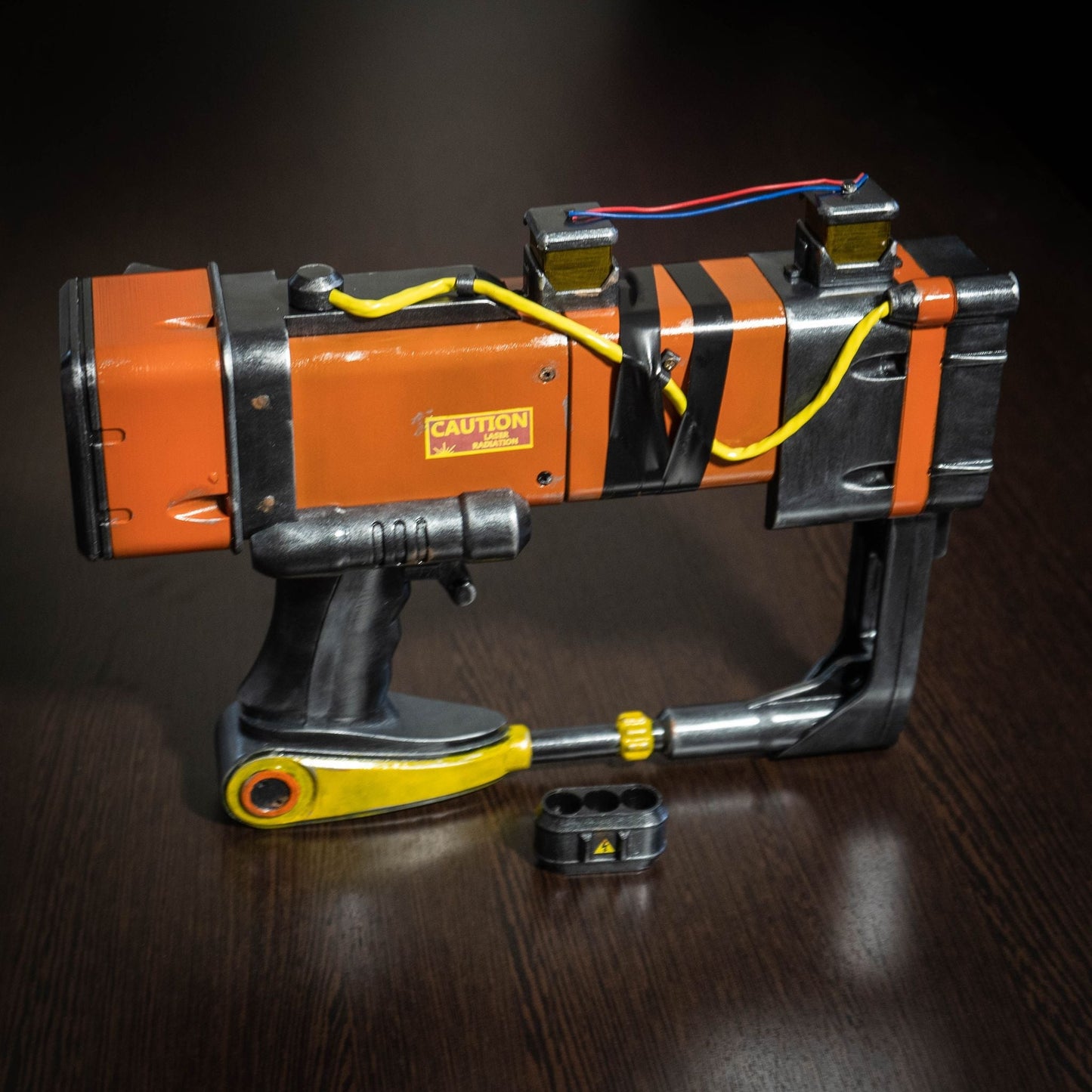 3D printed Fallout New Vegas AEP-7 laser pistol cosplay prop with orange and black detailing and caution label.