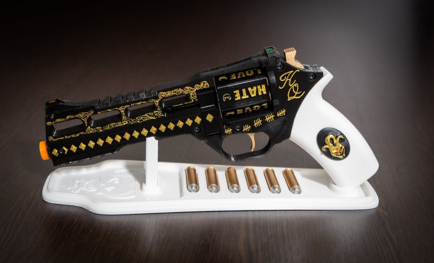 Harley Quinn's Revolver 3D printed black and white movie-accurate replica with gold detailing and six bullets on a white stand for cosplay.