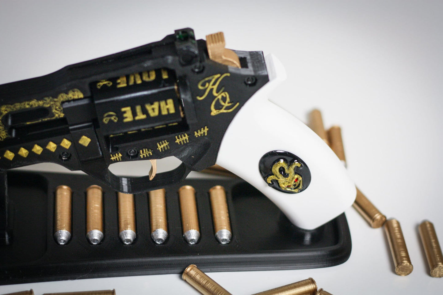 Harley Quinn's Revolver 3D printed movie-accurate cosplay prop with white grip and gold-accented black frame on display stand with bullets