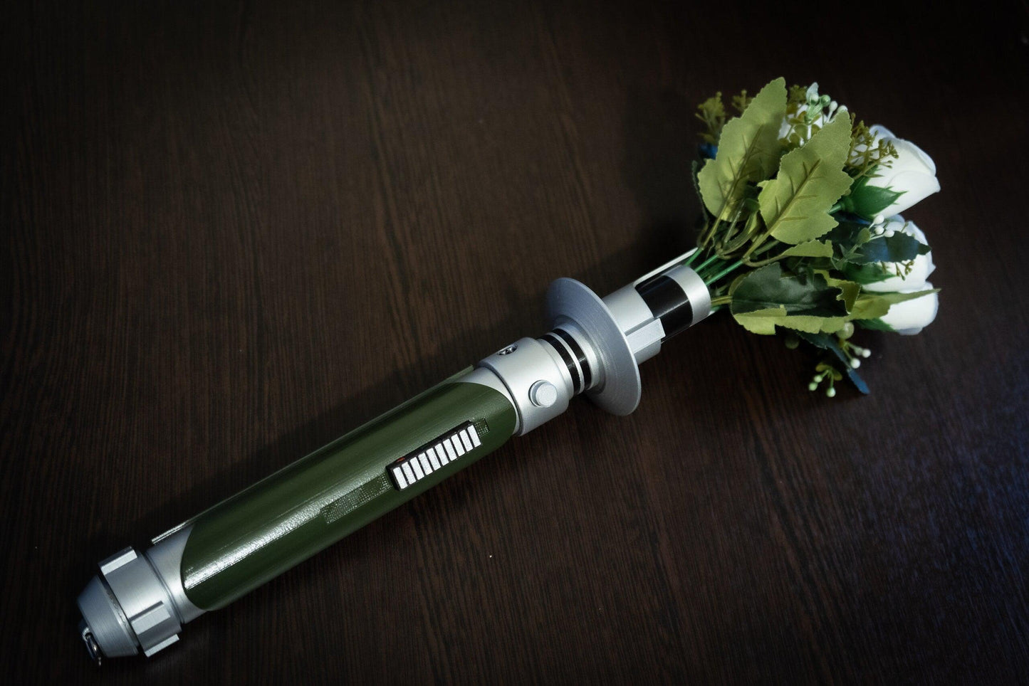Star Wars inspired bridal bouquet holder resembling Kanan Jarrus lightsaber with white flowers and green leaves on a dark wooden surface