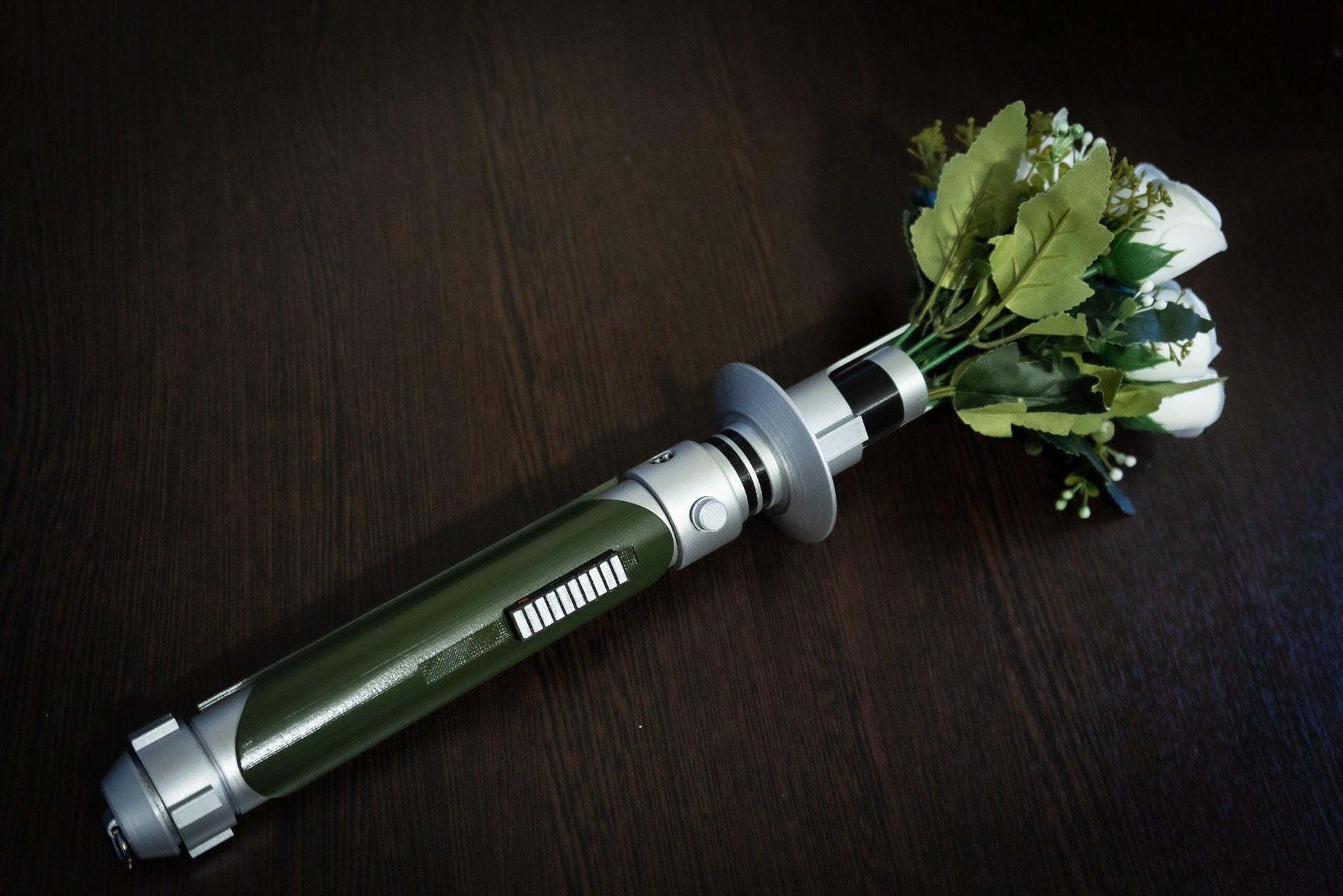Star Wars inspired bridal bouquet holder resembling Kanan Jarrus lightsaber with white flowers and green leaves on a dark wooden surface