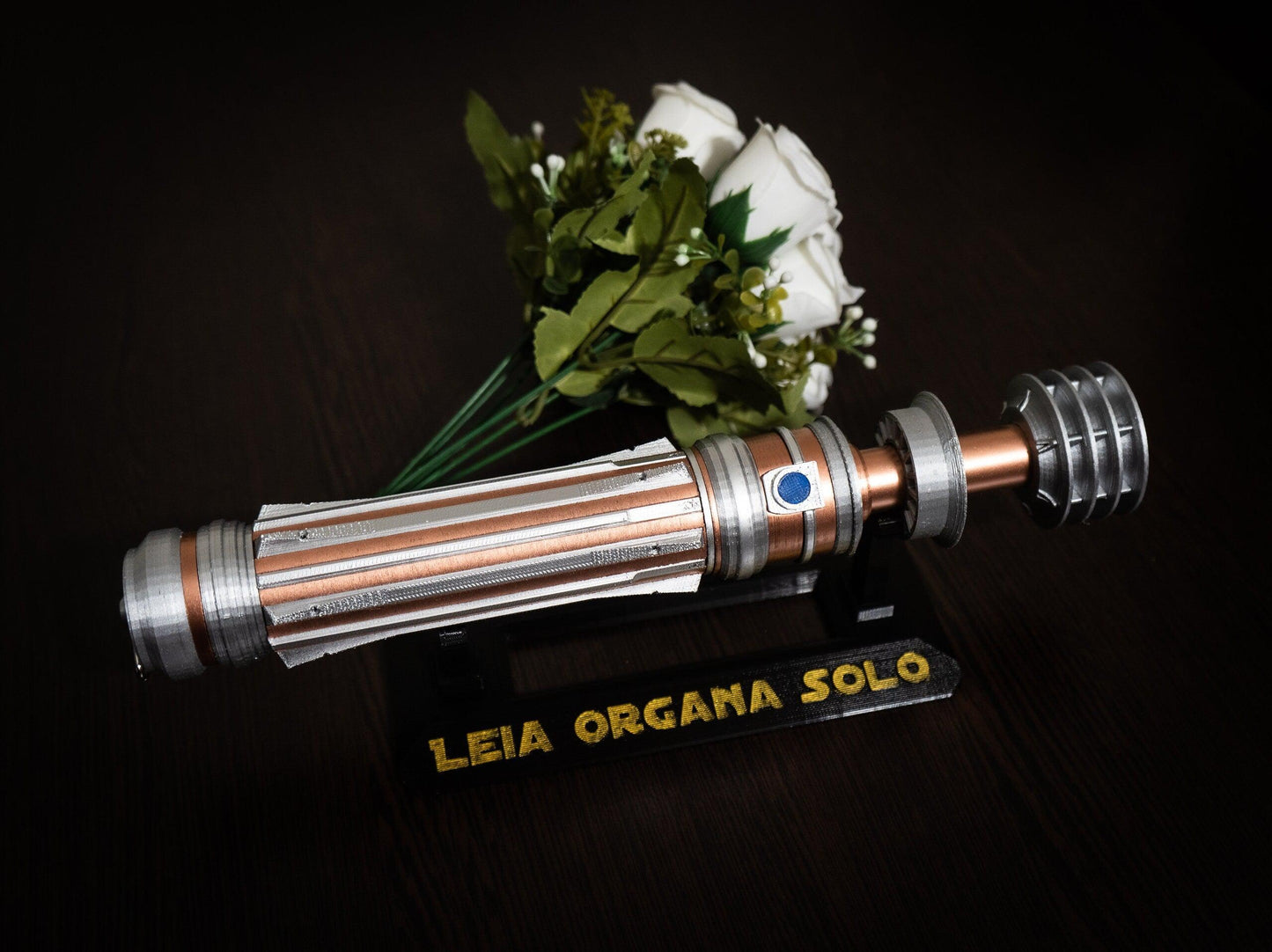 Star Wars inspired bridal bouquet holder shaped like Leia Organa's lightsaber hilt in copper and chrome colors with a wedding bouquet and display stand.