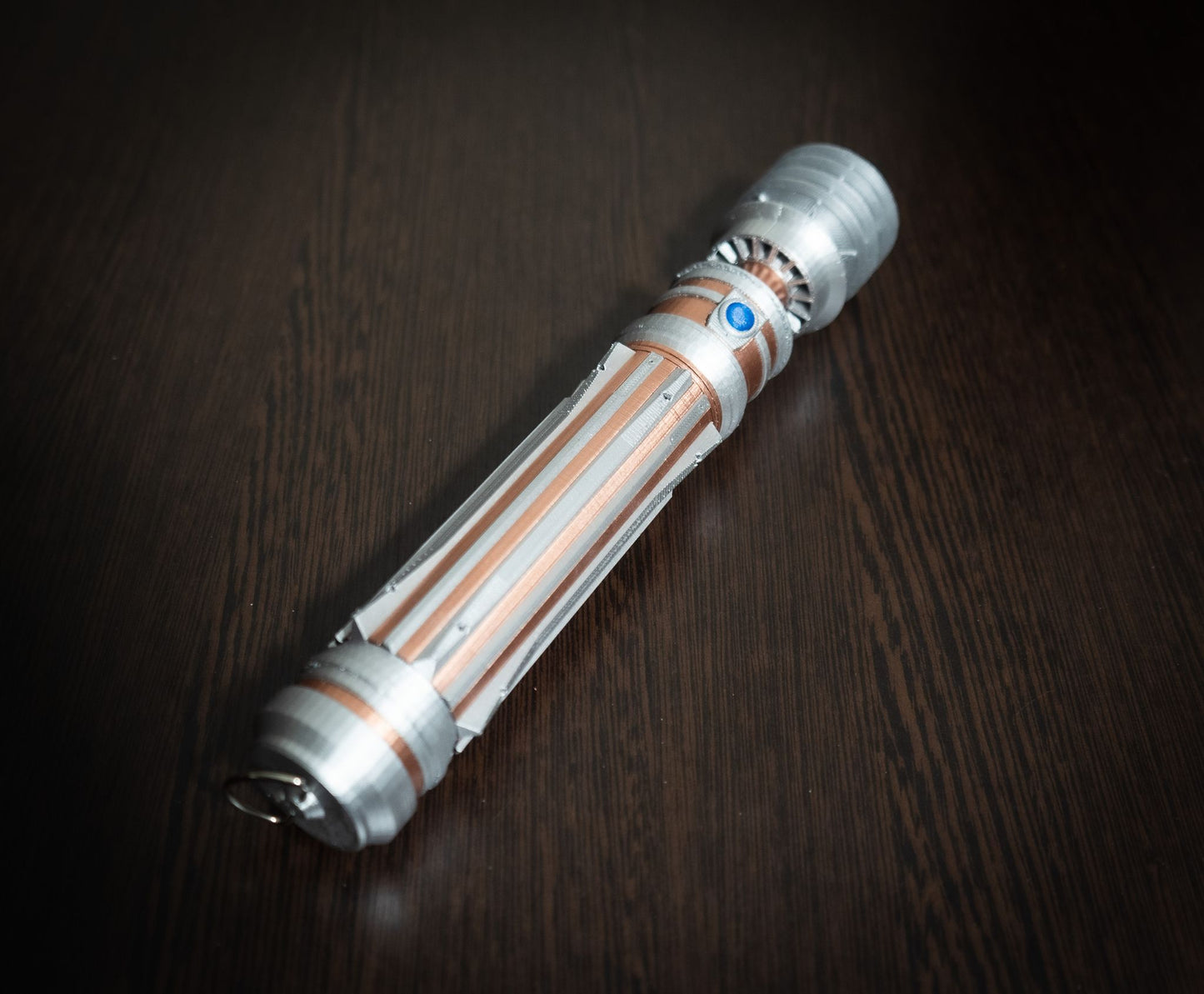 Star Wars inspired bridal bouquet holder designed like Leia Organa's lightsaber hilt in silver and copper colors on a dark wood surface