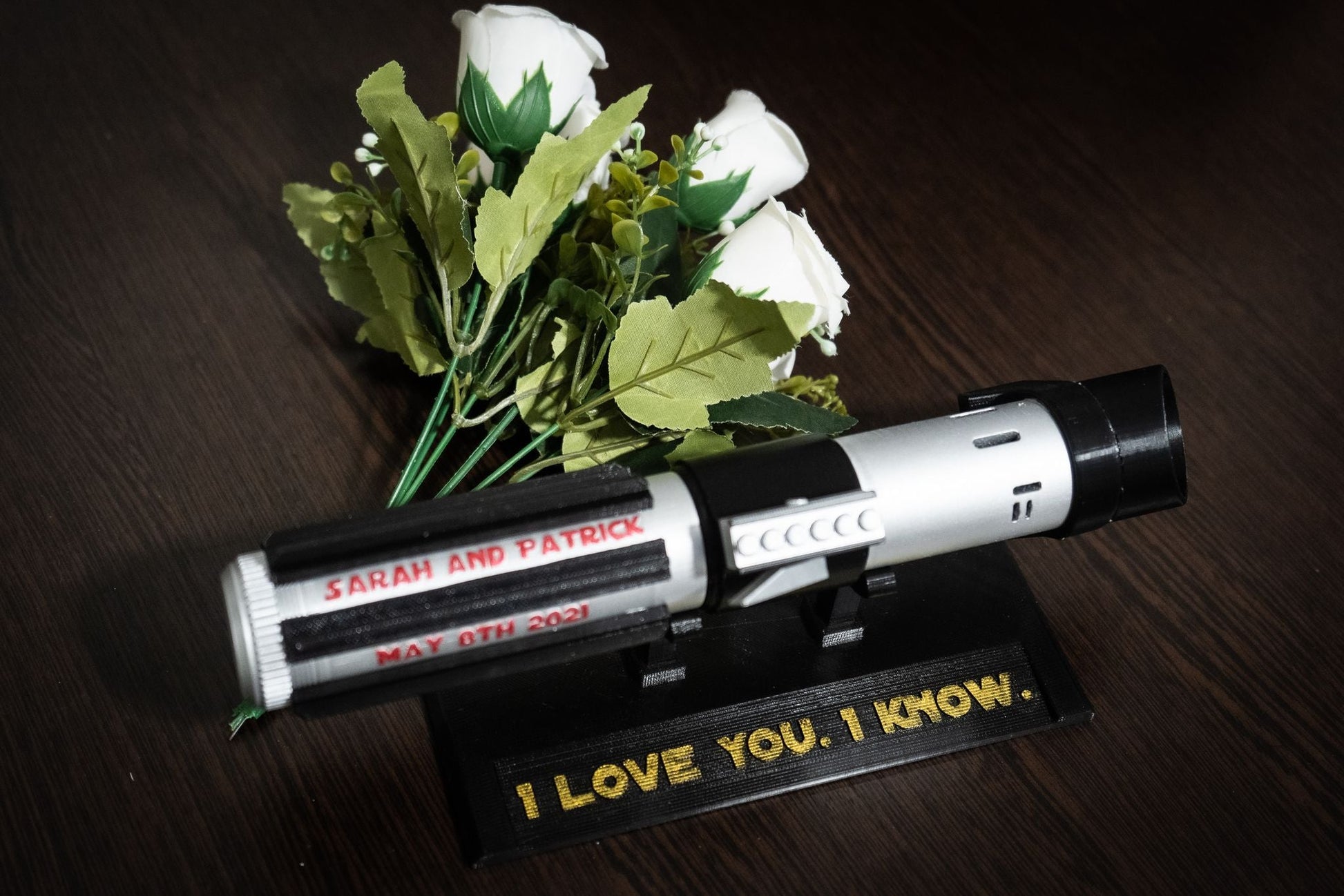 Star Wars inspired Darth Vader lightsaber bridal bouquet holder with custom engraved names and date, displayed with white roses.