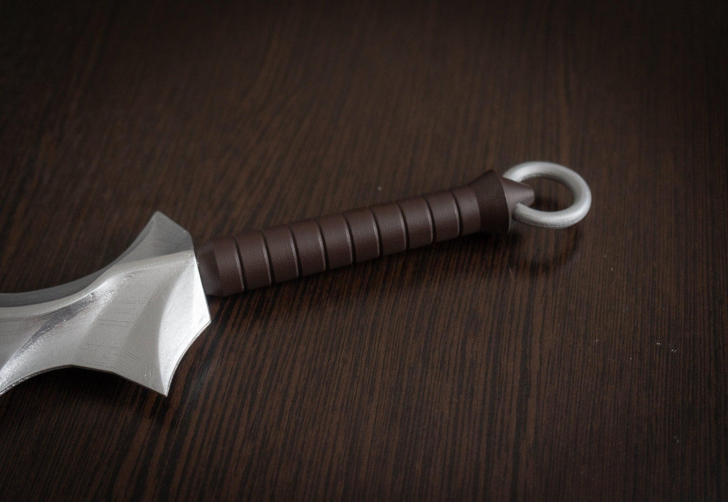 Close-up of brown handle and silver ring on Vampire Blade cosplay prop replica on dark wooden surface