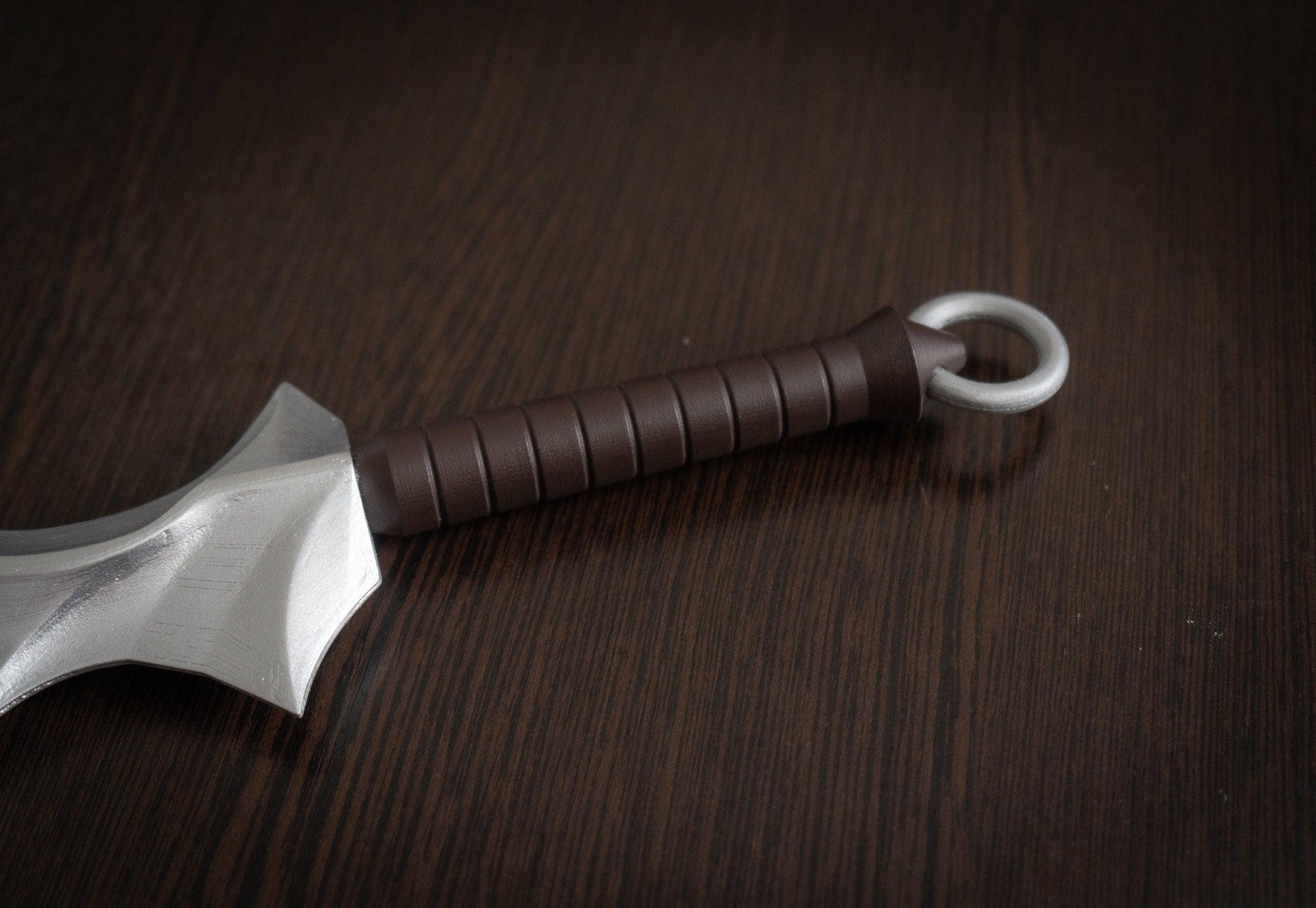 Close-up of brown handle and silver ring on Vampire Blade cosplay prop replica on dark wooden surface