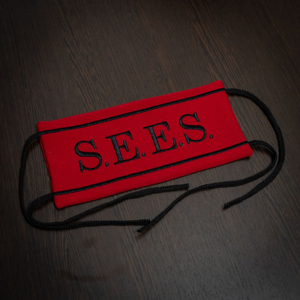 Red face mask with 'S.E.E.S.' branding on a dark wooden surface