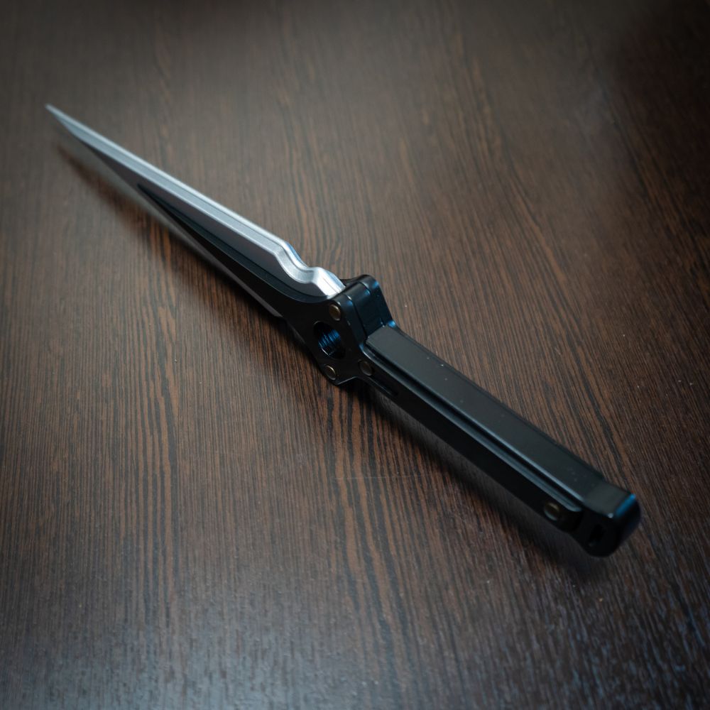 Futuristic knife with a metallic blade and black handle on a wooden surface